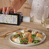 Person pouring olive oil over a salad with a bottle labeled 'Bona Furtuna' - olive oil subscription gift