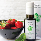 Bottle of Bona Furtuna basil-infused olive oil with a bowl of strawberries on a white background
