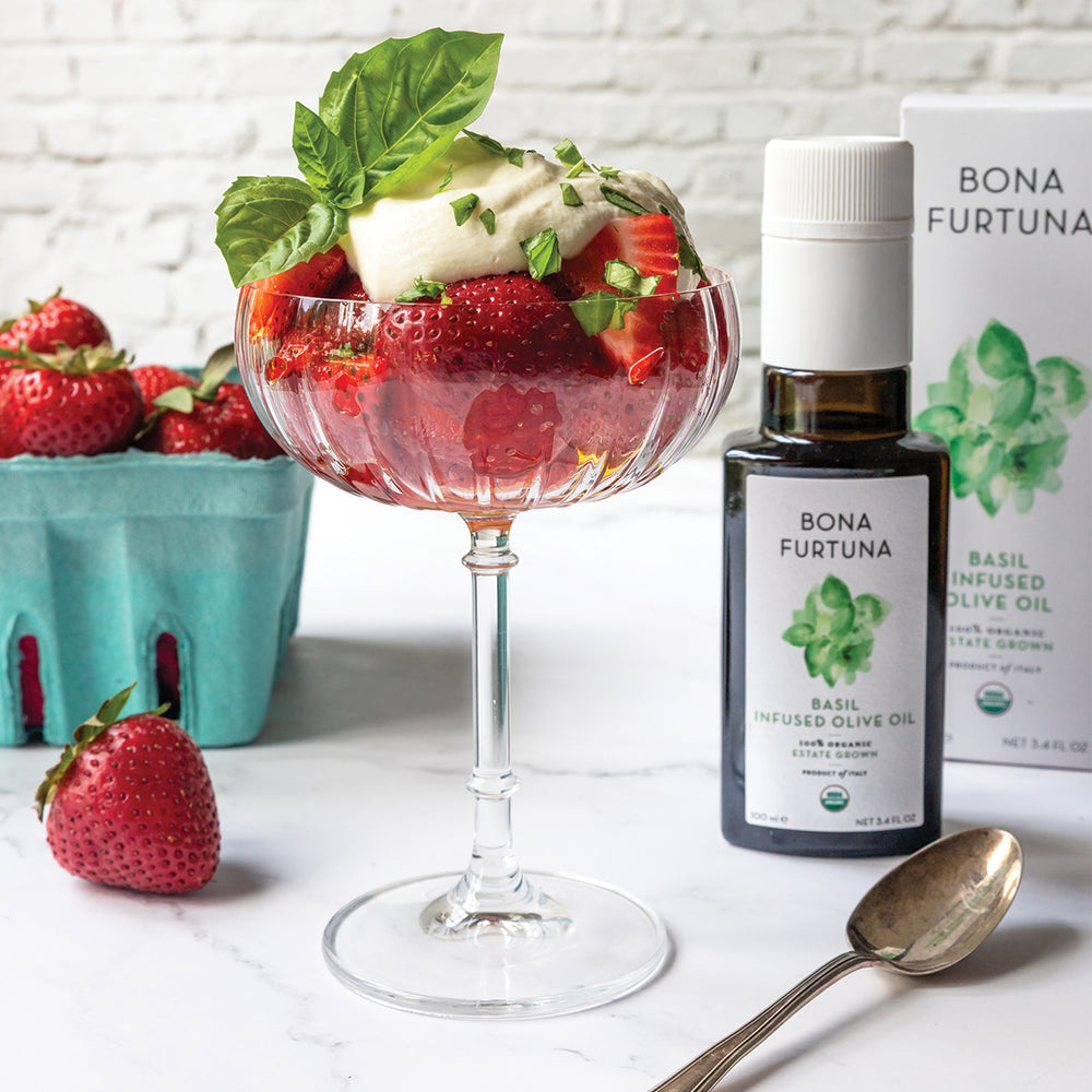 Strawberry dessert with basil leaves, a bottle of Bona Furtuna basil-infused olive oil, and a box of the product on a white surface.