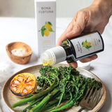 olive oil subscription box - Bottle of Bona Furtuna olive oil being poured over a dish of greens and lemon.