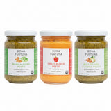 Three glass jars of Bona Furtuna pesto sauce on a white background: Basil Almond Pesto with green labeling, Sweet Pepper Pesto with a red-orange label, and Wild Fennel Almond Pesto with green labeling.